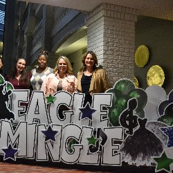 After Prom sponsors pose behind the "Eagle Mingle" yard sign